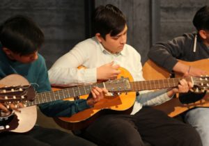 3 teenage kids playing guitar